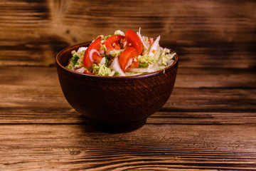 Dietary salad with the chinese cabbage and tomatoes in ceramic bowl on a wooden table