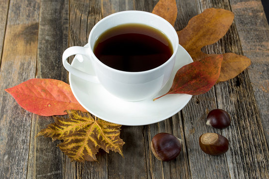 black coffee in white cup on saucer with autumn leaves and chestnuts on rustic wood