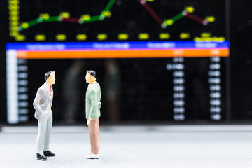 Miniature people : small figures businessmen stand and look at Stock Exchange Board Background with copy space and using as background finance business team competition concept, business plan concept.