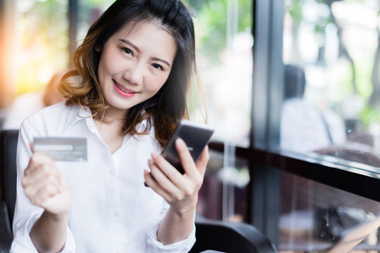 business asian girl in white shirt with credit card and smartphone onine shopping ideas concept with background of blur image coffeeshop