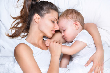Fototapeta na wymiar young beautiful mother hugs with her sleeping little cute son on white linen