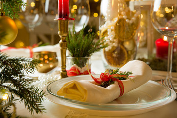 Beautiful served table with decorations, candles and lanterns. Little gingerbread house with glaze on white tablecloth. Living room decorated with lights and Christmas tree. Holiday setting close up