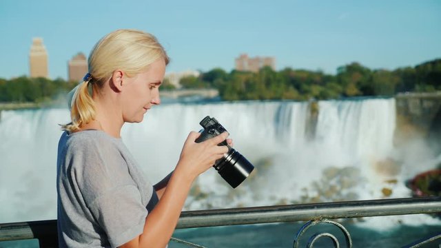 A woman looks through the photos on the camera screen. Against the background of a beautiful waterfall. Excellent memory of the holiday