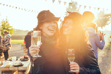 Two happy young women outdoors drinking white wine having fun in countryside