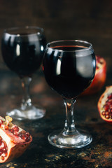 Fresh pomegranate wine in glass on black rustic surface.
