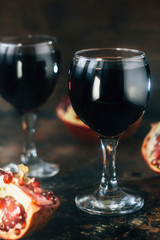 Fresh pomegranate wine in glass on black rustic surface.