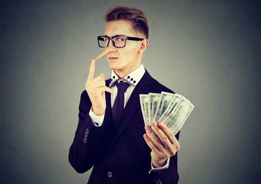 Financial fraud concept. Liar business man in suit and glasses with dollar cash
