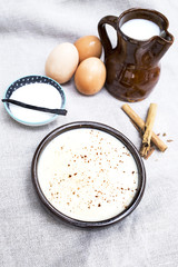 natillas en  tarrina de barro junto con los ingredientes como leche,azucar,canela y huevos
