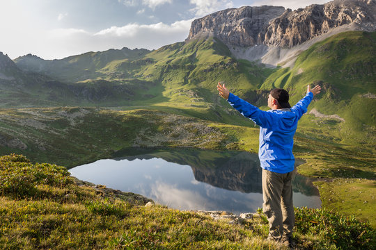 Hiker standing with raised hands near the beautiful mountain lake and enjoying view