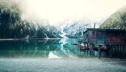 Gebirgssee vor verschneiter Alpenlandschaft mit Holzhütte im Vordergrund