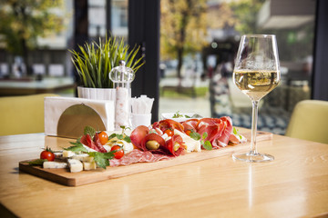Antipasto platter cold meat plate with grissini bread sticks, prosciutto, slices ham, beef jerky, meats, sausages, salami, ham, olives, laid, arugula and white wine on cutting board 