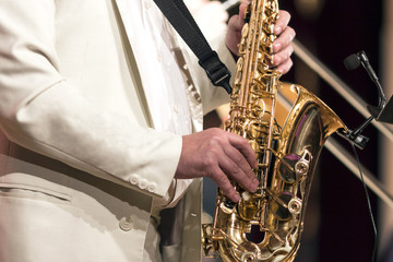 Obraz premium The saxophonist in a white suit plays solo on a saxophone. Close-up.