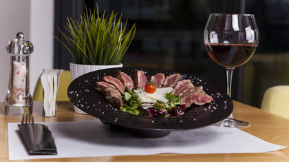 Juicy rib eye beef steak medium rare with spices cut in slices on slate plate with fried garlic and spinach salad. dark style, view from above, close-up