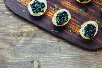 Top view of black caviar appetizers at wooden board.