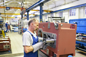älterer Mechaniker montiert Getriebe im Maschinenbau // industrial worker assembles gearboxes in...