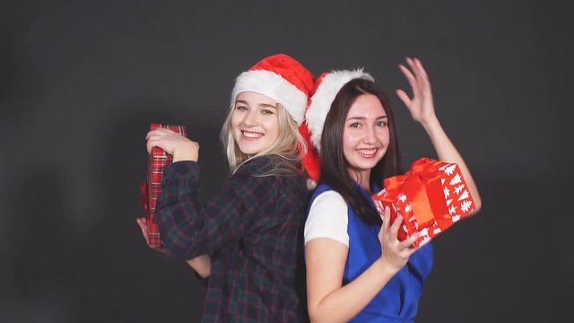 Two attractive girls with Christmas gifts in hands laughing and dancing looking at camera.