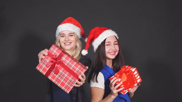 Two attractive girls with Christmas gifts in hands laughing and dancing looking at camera.