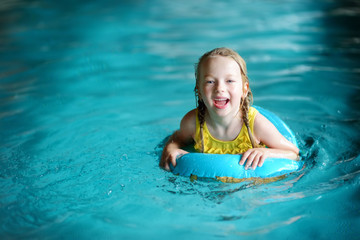 Cute little girl playing with inflatable ring in indoor pool. Child learning to swim. Kid having fun with water toys.