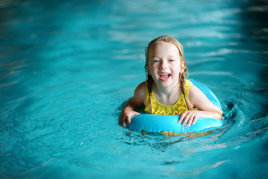 Cute Little Girl Playing With Inflatable Ring In Indoor Pool. Child Learning To Swim. Kid Having Fun With Water Toys.