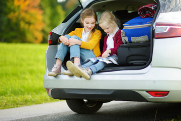 Two adorable little girls ready to go on vacations with their parents. Kids sitting in a car examining a map.