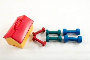 A red and yellow toy house depicting a gym. Dumbbells for children are folded in the form of indicia. The concept of a path to sport.