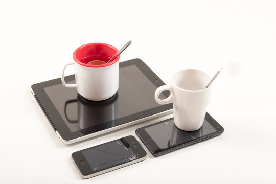 The smartphone and tablet are used as a stand for cups with tea. Toy set of dishes. Broken phone.