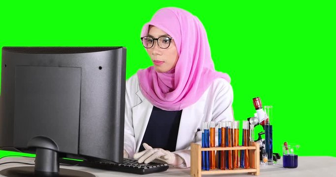 Muslim scientist working typing on a computer and smiling at the camera with test tube on the table. Shot in 4k resolution with green screen background