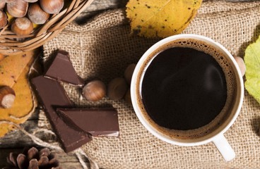 black coffee on wooden table with chocolate , hazelnuts, and fallen leaves decoration. on wooden table. top view