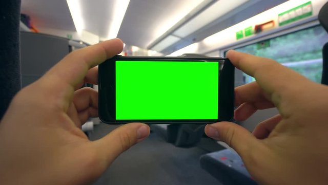 Hands holding (using) a smapthone with a green screen on the train. Close-up shot