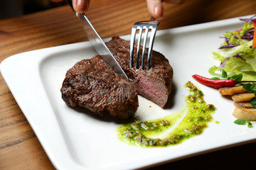 Hands cut medium rare beef steak with green dressing sauce pepper mushrooms and salad 