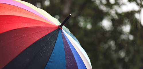 Panorama of close-up  umbrella in rainbow colors in rainy autumn day, blur focus