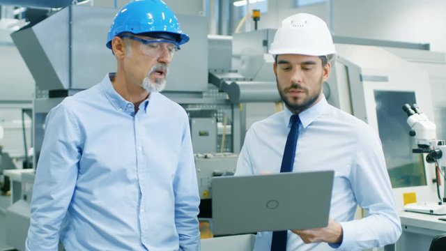 Head of the Department Holds Laptop and Discusses Product Details with Chief Engineer. They Wear Hard Hats and  Work in the Modern Factory. Medium Shot. Shot on RED EPIC-W 8K Helium Cinema Camera.