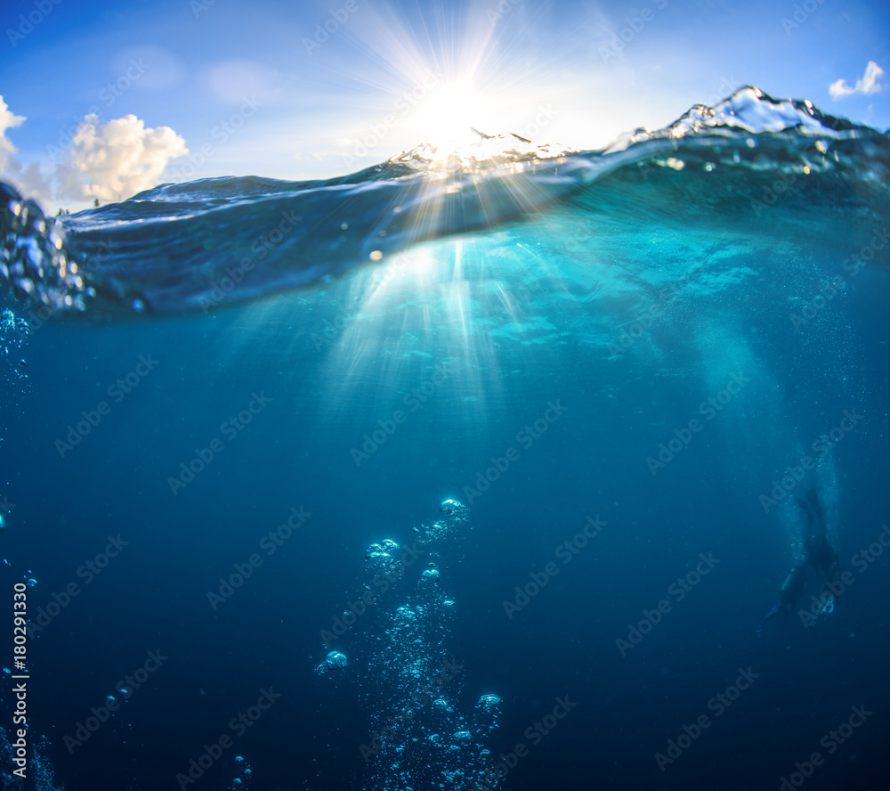Wall mural underwater scenery, deep blue water of the ocean, air bubbles, waterline splitting skyline, divers d