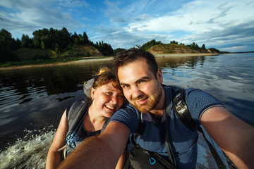 Selfie of happy couple during riding on motor boat. Beautiful riverside on background