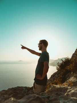 Young Man Standing on top of a Cliff, pointing into the distance