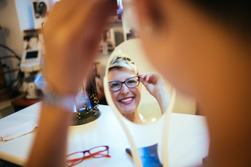 Fototapeta na wymiar Beautiful middle age woman choosing a glasses in optician store.