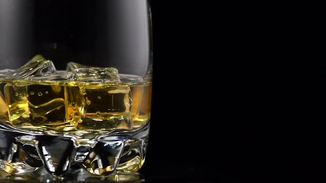 Whisky on the rocks. Glass of whiskey with ice isolated on black background. Rotation 360 degrees. 4K UHD video 3840x2160