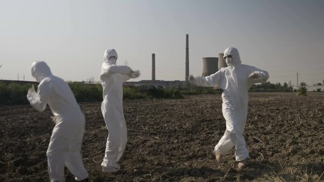 Funny scientists in hazmat suits dancing and fooling around near the location of a refinery celebrating successful mission