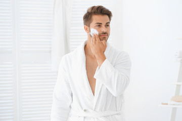 Young man applying facial cream in bathroom