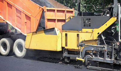 Road construction. Applying new hot asphalt using road construction machinery and power industrial tools. Roadworks repaving process.