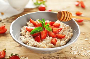 Delicious oatmeal porridge with strawberries in bowl on table