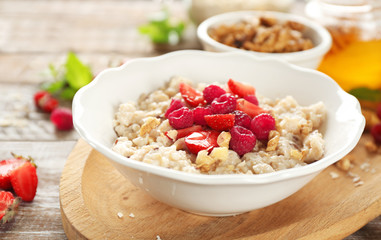 Delicious oatmeal porridge with strawberries and raspberries in bowl on table