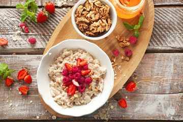 Delicious oatmeal porridge with strawberries and raspberries in bowl on table