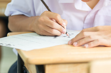 Asian Boy Students taking exams, writing examination room with undergraduate students inside. Student sitting learning lessons on row desk chair doing final exam in classroom with uniform.