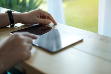 Closeup image of a woman's hands pointing , touching and using tablet pc  on wooden table in cafe
