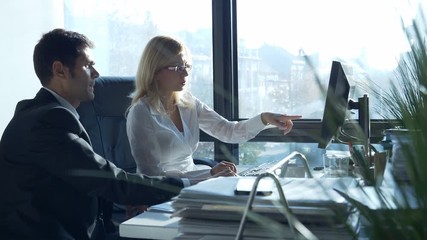 Two business professionals, man and woman, working together in office, looking at data on computer / Business professionals working together - Powered by Adobe