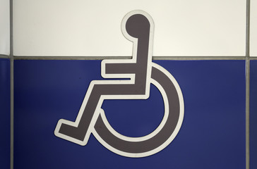 Grey wheelchair sign on the a white and blue wall. Public restroom signs with a disabled access symbol.