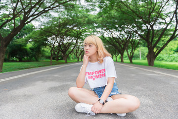 Portrait of asian young girl sit on the road at tunnel trees,Beautiful thai woman take a photo outdoors,golden hairs