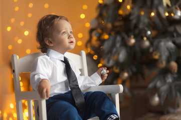 Happy little boy sitting near the luxury decorated Christmas tree in gold colors. New Year's holidays with family. 