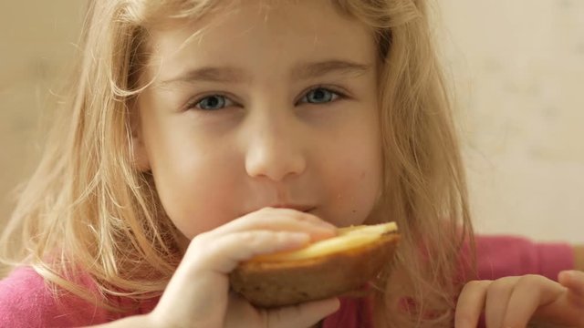 A little girl is eating a sandwich with cheese. The child eats bread and cheese.